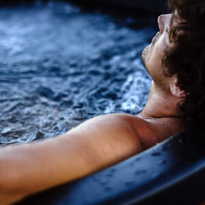 Close up of man in hot tub relaxing with his head back on the side and his eyes closed.